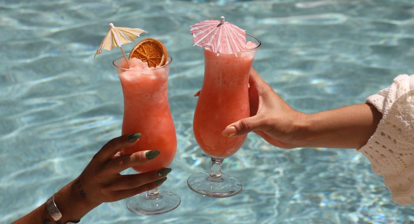 two cocktails raised in a toast over the pool
